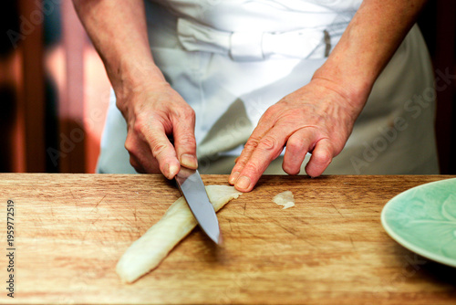 Obraz na plátně Hands slicing a vegetable with a knife on a wooden cutting board