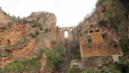 Cinematic low-angle shot of the iconic Puente Nuevo bridge and vertical limestone cliffs in Ronda, Andalusia. Featuring historic ruins and the dramatic Tajo gorge landscape.