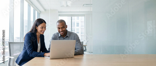 Cheerful diverse business professionals using a laptop at a desk in a bright office. Wide banner with right copy space