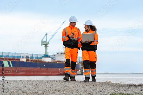 Logistics Supervisors in Safety Uniforms Discussing Operations Near Cargo Ship at Sea Port, Diverse Team of Maritime Engineers in High-Visibility Gear Walking at Industrial Terminal