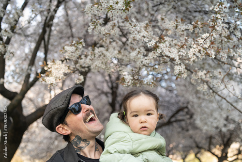 Photos A young hipster father smiling portrait with his young daughter by the blossomin