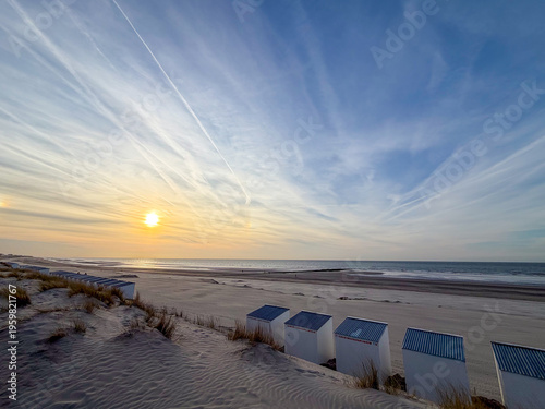 Colorful beach huts at sunset on Nieuwpoort beach, Belgium with dramatic sky and golden light reflecting on ocean waves