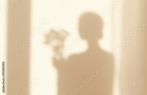 Shadows silhouette woman waking up in morning at home sunset or dawn in the rays the sun reflected on wall holding a bouquet of flowers in her hands. Golden hour through window curtains. Blurry.