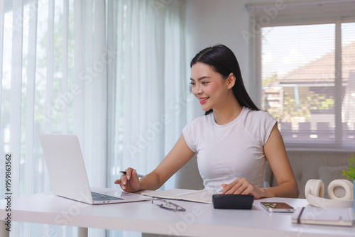 Young woman working remotely, typing on laptop, writing in notebook. Concept of female student studying online education