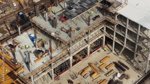 Drone footage capturing a partially completed multi story concrete building with scaffolding, formwork, and materials, highlighting structural progress and active construction environment.