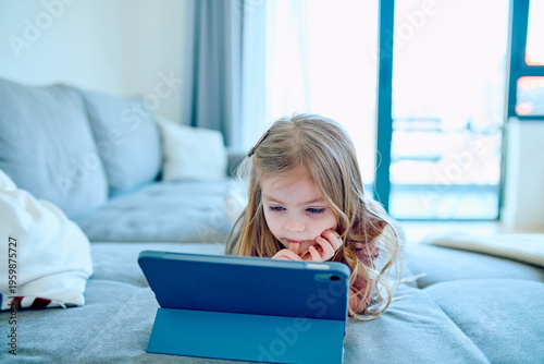 Obraz na plátně Young girl lying on a sofa, engrossed in digital learning or entertainment on a tablet