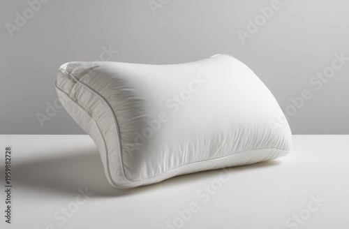 A close-up studio shot showcases a uniquely shaped white pillow, resting on a reflective surface against a soft gray backdrop