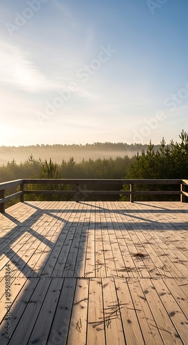 Sunrise over a wooden observation deck overlooking a misty forest landscape with pine trees and a clear sky