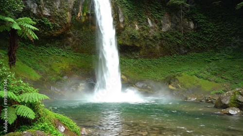 Waterfall cascading down rocky slope surrounded by lush greenery.