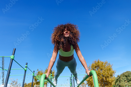 Photos Athletic woman with curly hair performing bodyweight exercises on parallel bars