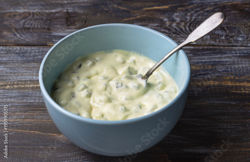 Homemade tartar sauce with pickles in light blue bowl on wooden background, creamy condiment with spoon