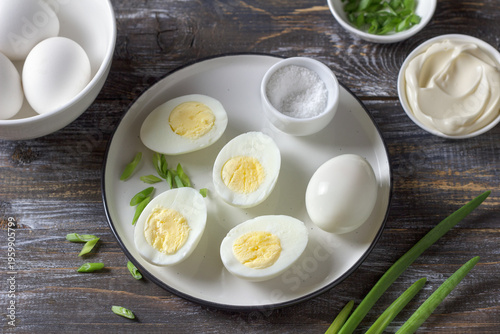 Boiled eggs with green onion, salt and mayonnaise on plate over wooden table