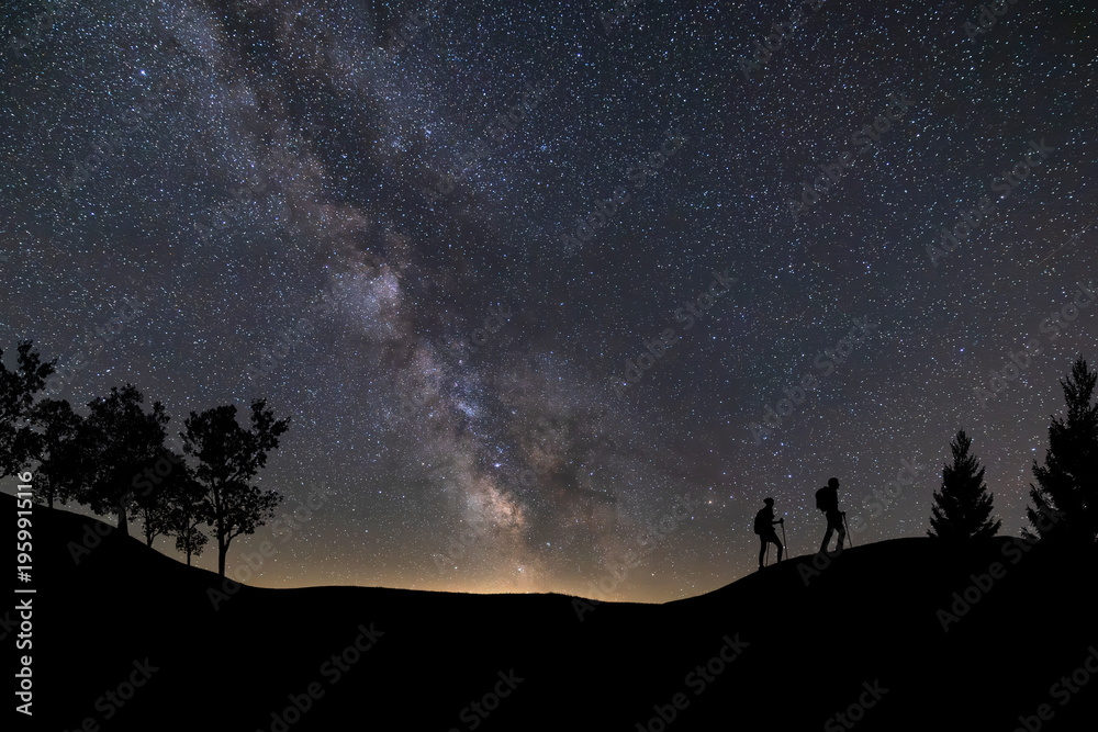 Fototapeta premium Lone person standing on top of rock, pointing with hand towards the Milky Way and the vast expanse of universe. Stunning silhouette of man gazing out into the cosmos. Power of dreams and aspirations.
