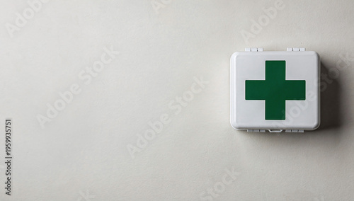 White plastic first aid box with a green cross on a smooth white wall in horizontal right-aligned framing.