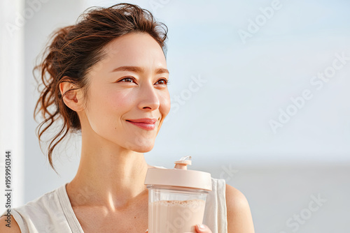 Pretty natural looking woman with curly hair smiles while holding protein shake container. background features bright, airy setting, enhancing her joyful