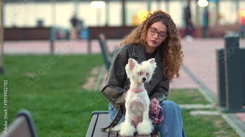 Young woman caressing her cute white dog on a park bench
