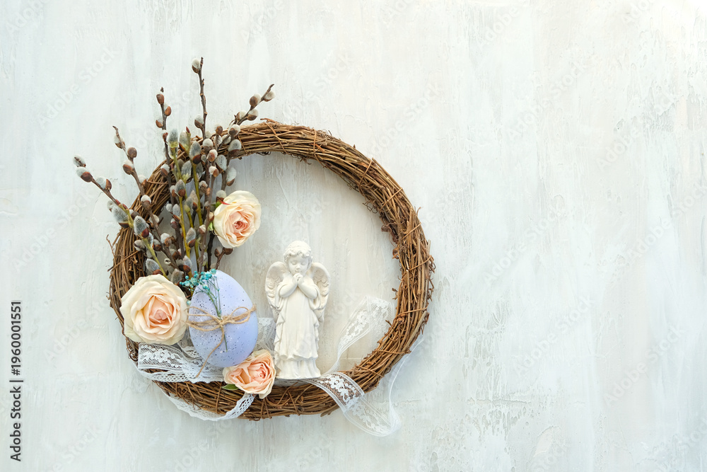 Obraz premium Easter holiday background. Beautiful easter wreath with angel figurine, egg and rose flowers on light table close up. symbol of Easter, Christianity religion, faith in God, prayer. flat lay.