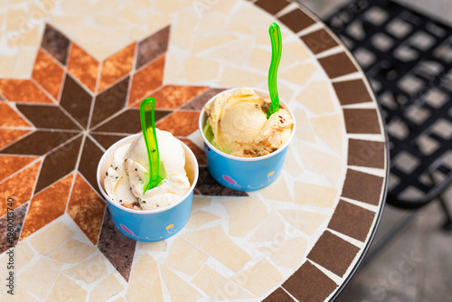Top view flat lay of paper cups filled with colorful ice cream scoops on a cafe table. Overhead perspective of a refreshing sweet summer dessert with negative space