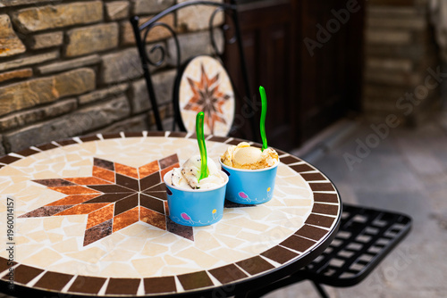 Gelato in disposable eco friendly paper cups placed on a cafe terrace table. Summer outdoors lifestyle featuring sweet cold dessert and natural daylight