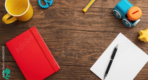 Rustic timber table showcasing a vibrant yellow cup, fun toys, bold red notebook, crisp white paper, and trusty pen