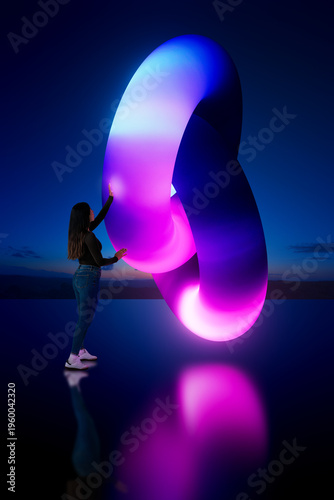 Latin woman touching glowing 3D abstract loop structure with gradient light in dark environment