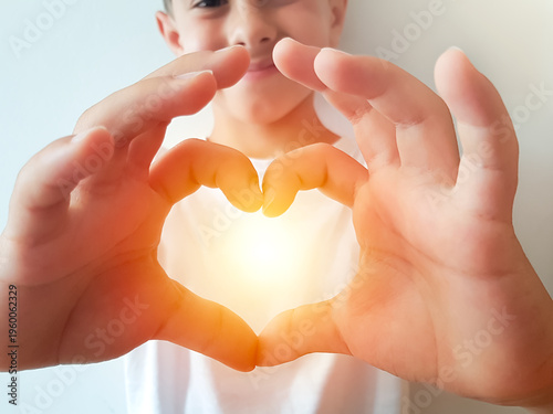 Young child's hands making a heart shape with warm glowing light inside.