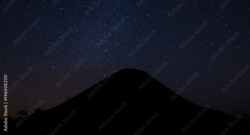 Fototapeta premium Dark silhouette of a volcano erupting under a sparkling night sky