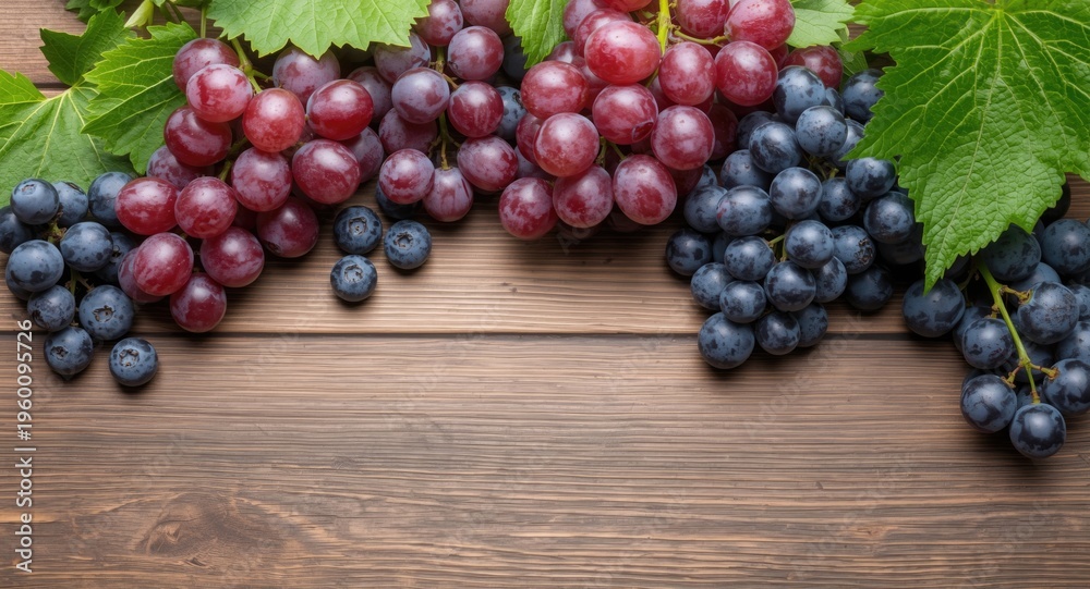 Naklejka premium Fresh red grapes and blue grapes with green leaves on wooden table copy space