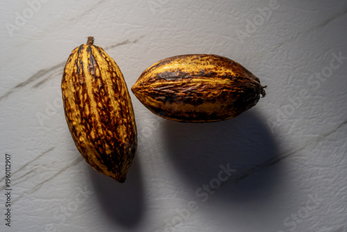 Mazorca de cacao entera sobre superficie de mármol blanco con iluminación dramática