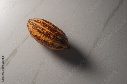 Mazorca de cacao entera sobre superficie de mármol blanco con iluminación dramática