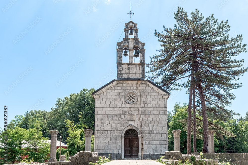 Fototapeta premium Symmetric view of the Court Church on Cipur in Cetinje, Montenegro. Stone Orthodox chapel with a prominent belfry surrounded by ancient ruins and pine trees in Europe