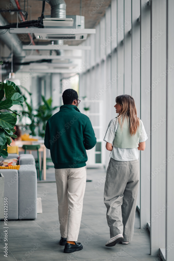 Obraz premium Diverse coworkers walking and talking in office hallway