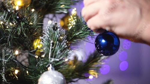 Hands of a man close-up decorate the Christmas tree for Christmas or New year. He hangs a blue ball toy on the tree.