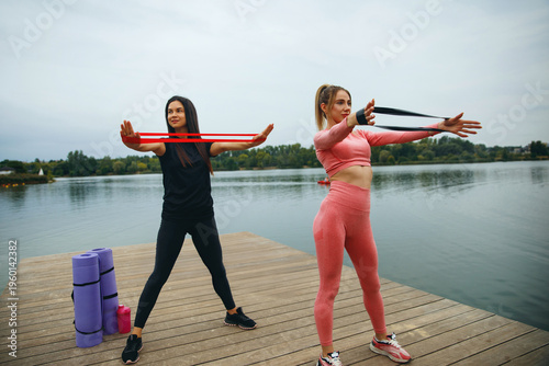 Women Practicing Yoga Exercises With Resistance Bands by the Lakeside During a Cloudy Day for Health and Wellness