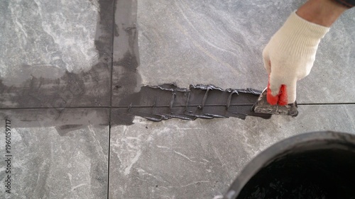 Schilderij op canvas Close up of a worker's gloved hand using a trowel to apply dark grey grout between large stone-look floor tiles
