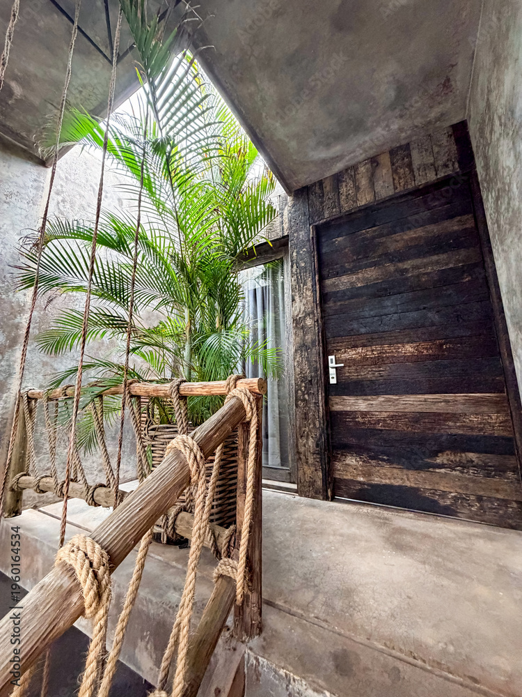 Obraz premium Indoor balcony with rope railing, lush palm and wooden door, low angle view