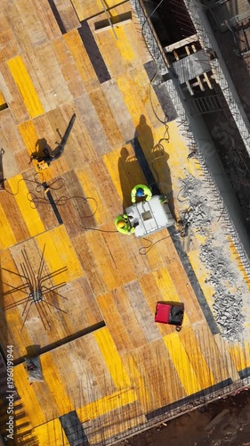 Aerial drone shot looking straight down at two construction workers installing steel reinforcement on formwork deck, showcasing structural preparation and active building process.