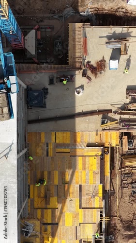 Aerial drone shot looking straight down at two construction workers installing steel reinforcement on formwork deck, showcasing structural preparation and active building process.