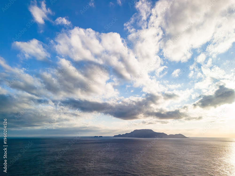 Obraz premium 沖に神津島が見える。 青い海と緑の森が美しい、式根島の空中ドローン撮影。 東京都伊豆諸島式根島-2025式根島は東京都心から南へ160km。 外周12kmの小さな有人島。 温かい黒潮が当たり水温と水質が高い。 また、リアス式の入り組んだ入り江が多く、海水浴や釣りが盛ん。 温泉島としても有名。海際に多くの無料露天風呂がある。 