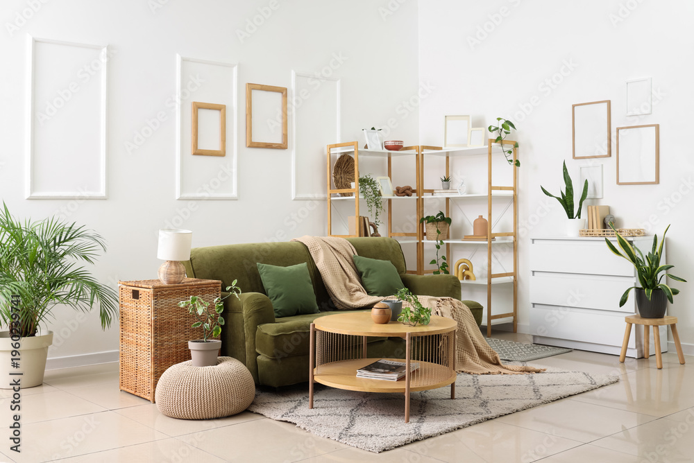 Fototapeta premium Interior of light living room with green sofa, shelf unit and plants