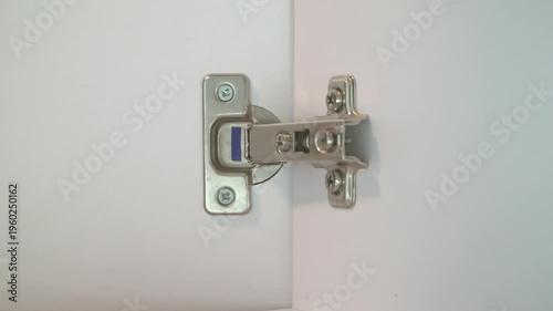 power tool bit turns a screw on a silver furniture hinge. This precise adjustment ensures proper alignment of white cupboard doors during assembly.