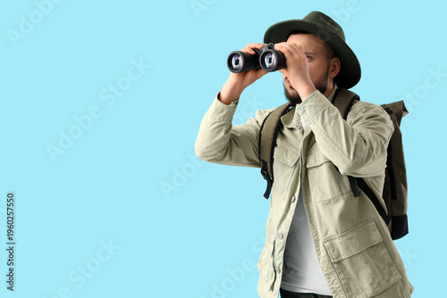 Male traveler looking through binoculars on blue background. Search concept