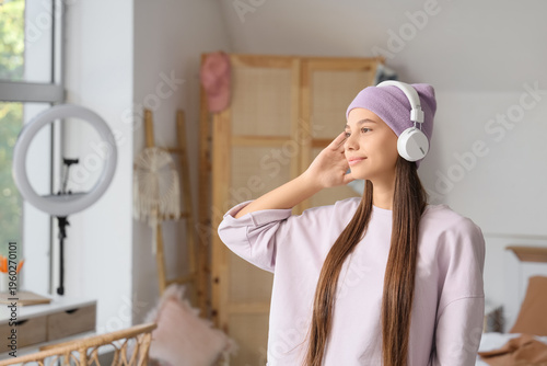 Teenage girl with headphones listening to music in bedroom