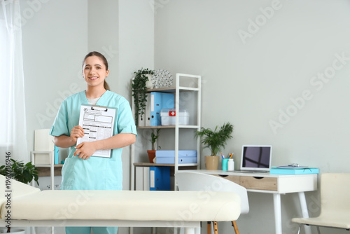 Young happy female doctor with clipboard near couch in clinic