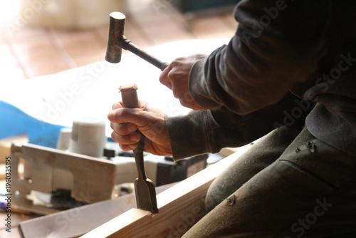 ノミで材木を削る男性
