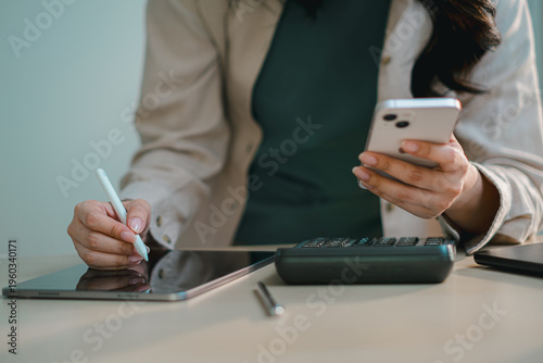 businesswoman using smartphone and tablet with calculator on desk, representing digital finance, accounting, online banking, budgeting, tax management and modern fintech workflow in office