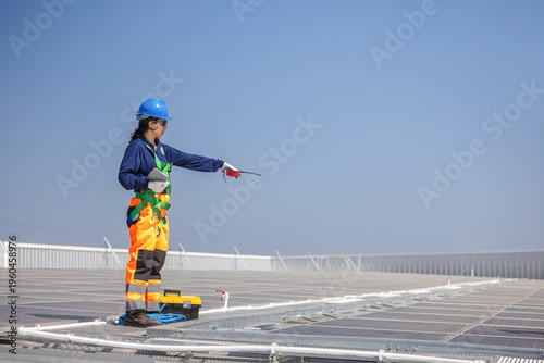 Engineer in safety harness inspecting solar panel installation on rooftop, Technician with walkie talkie during maintenance of photovoltaic system, Worker working on industrial solar power plant