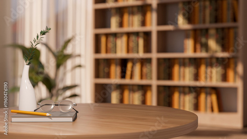 Eyeglasses and pencil on book with vase on round wooden table across bookshelf and window in library