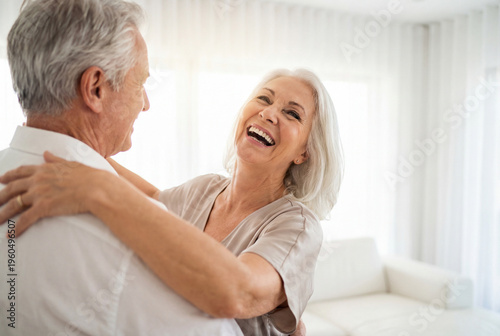Happy senior woman laughing while dancing with her husband in bright living room