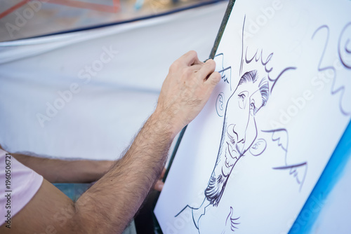 Slika na platnu Artist drawing a humorous caricature portrait on a white canvas with black ink